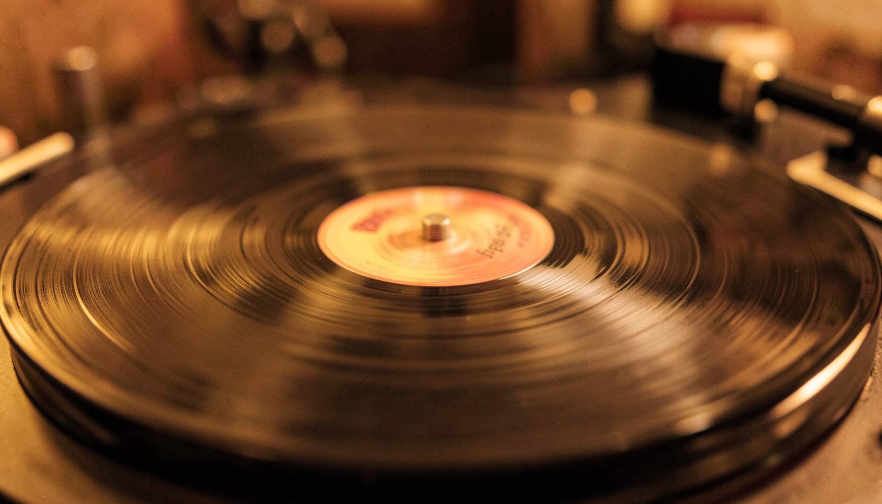 A close-up of a vinyl record spinning on a turntable, warm amber and brown tones, soft motion blur on the grooves