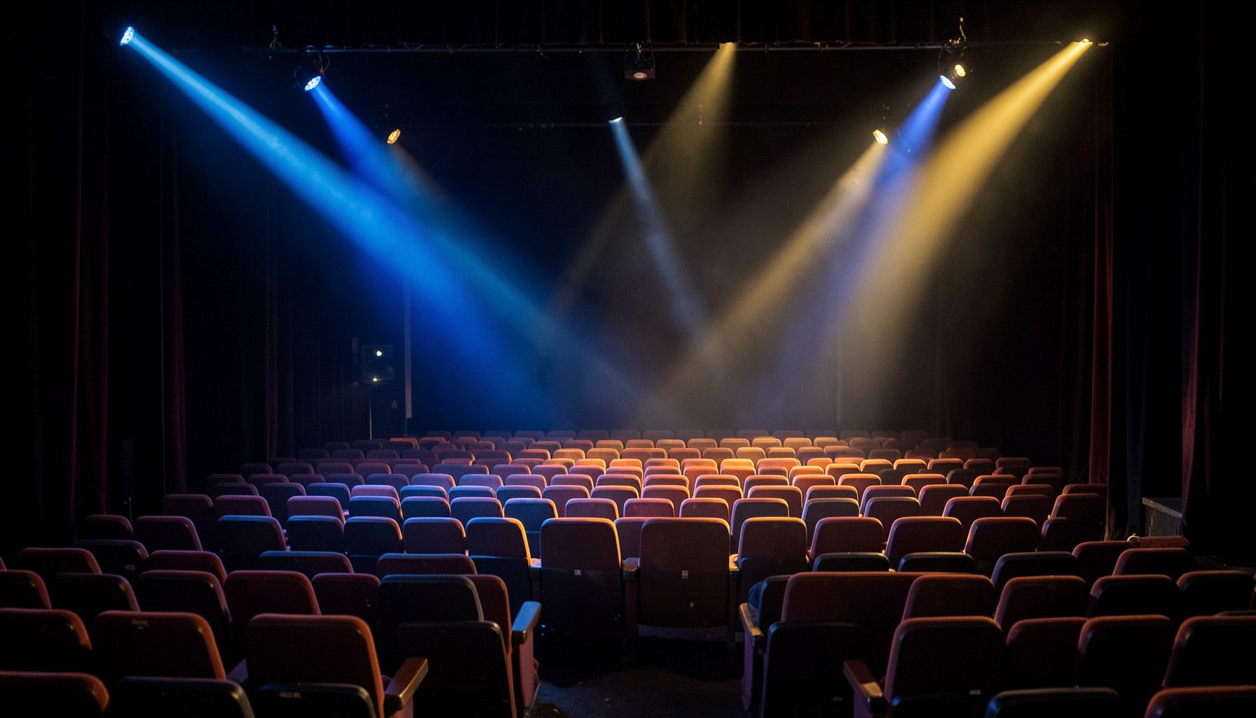 A colorful theater stage with empty chairs and soft spotlight beams crossing in blue and gold hues
