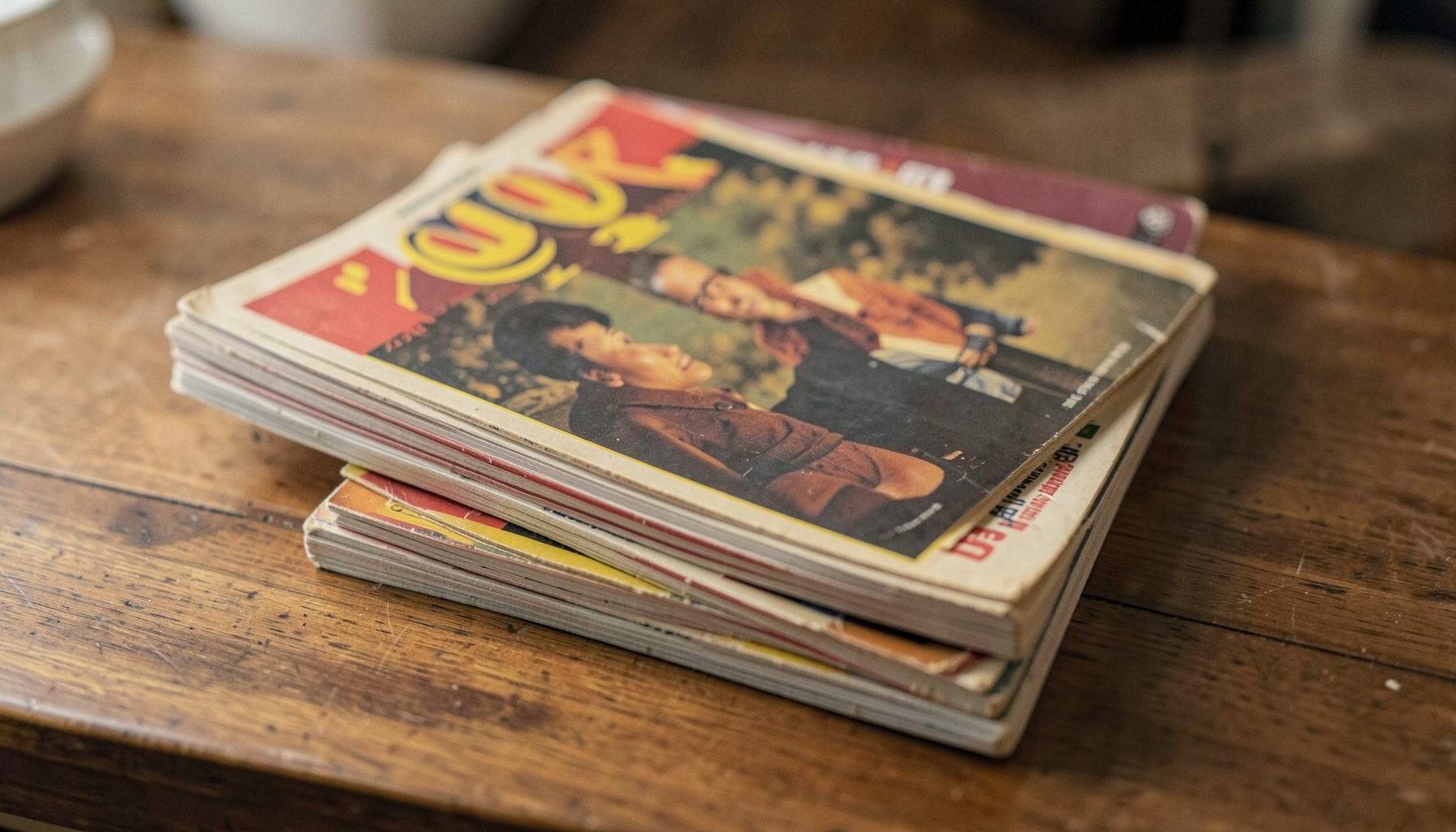 A stack of vintage music magazines on a wooden desk, muted earth tones with pops of red and yellow on the covers