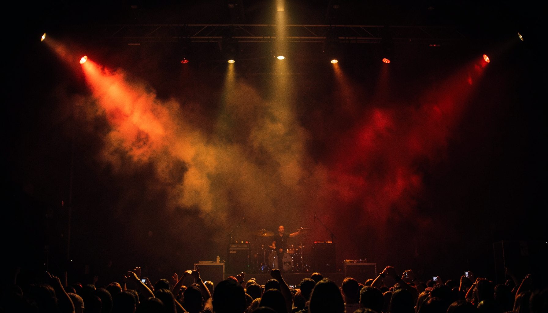 Dark stage with warm amber and red spotlights glowing through haze, moody concert atmosphere