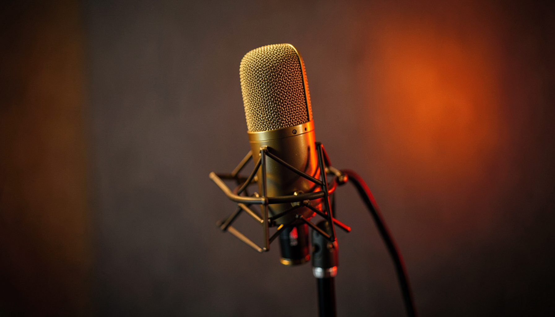 A warm-toned studio microphone on a stand, shallow depth of field, amber and dark gray background with subtle red accent glow
